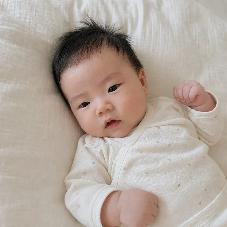 아기가 이불 위에 누워 카메라를 바라보는 사진